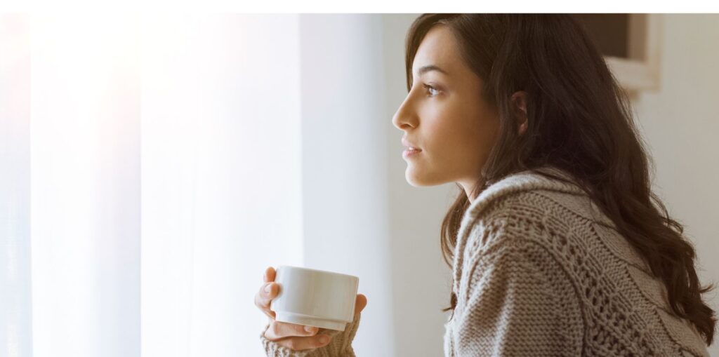 Woman with coffee looking out window.